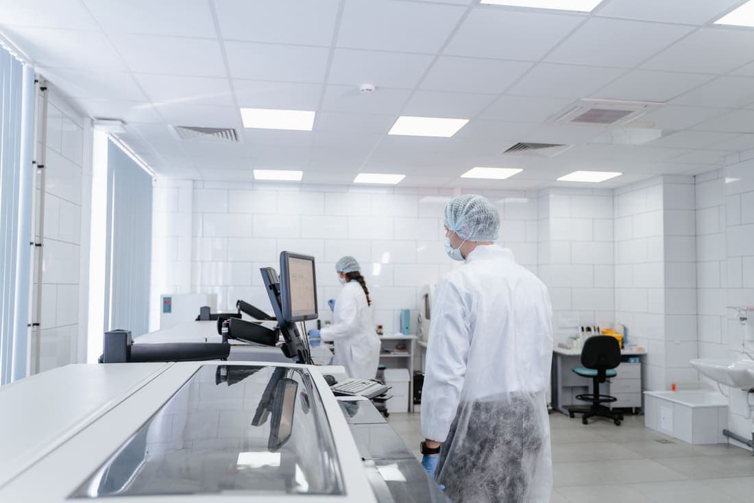 Pharmaceutical operators in cleanroom garb working at a packaging line workstation.